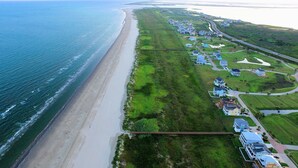 Luftaufnahme einer Küstenwohngegend mit Strand, Häusern und einer Straße.