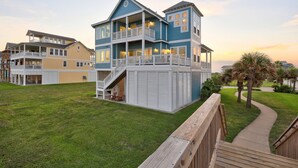 Ein mehrstöckiges Strandhaus mit Balkon, überdachter Terrasse und Holzterrasse.