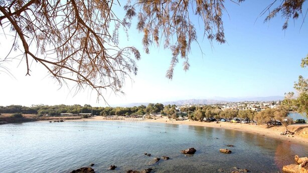Visão clara de um lago com pedras visíveis e uma cidade ao longe.