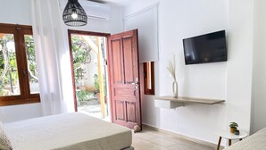 Quarto com duas camas, televisão, porta de madeira e uma pequena mesa com uma planta.