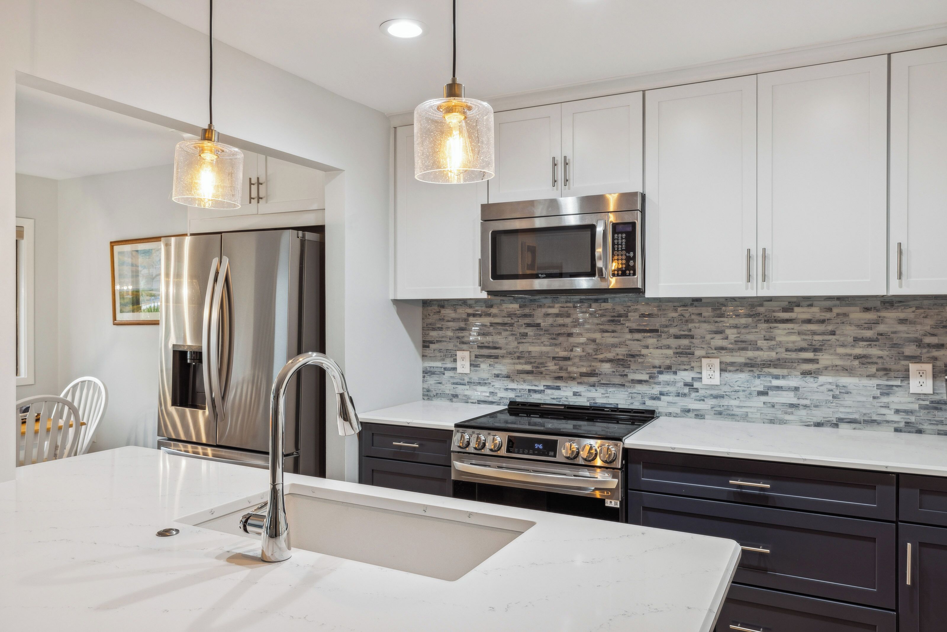 Una cocina moderna con electrodomésticos de acero inoxidable, una encimera blanca y un salpicadero con diseño de mosaico.