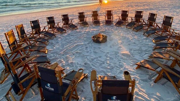 Sillas dispuestas en círculo alrededor de un brasero en la playa al atardecer.
