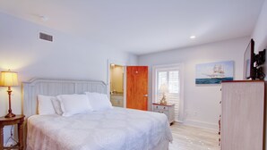 Une chambre à coucher avec un grand lit, une table de chevet, une commode, une porte, un tableau et une fenêtre.