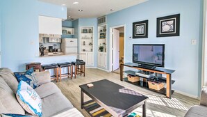A living room with a sofa, coffee table, TV, and kitchen area. - Corpus Christi Condo - Walk to Whitecap Beach! (Corpus Christi)