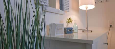 A bathroom with a white countertop, a mirror, a lamp, and a potted plant.