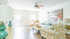 A spacious living room with hardwood flooring, a ceiling fan, a sofa, a patterned armchair, and a painting on the wall.