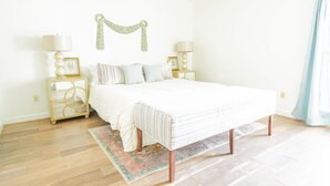 A bedroom with a large bed, two bedside tables with lamps, a decorative wall piece, and a light blue curtain.