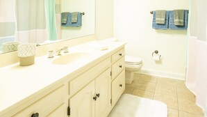 A bathroom with a white sink, mirror, and toilet. There are towels hanging on the wall and a shower curtain.