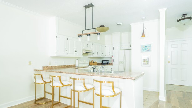 A kitchen with white cabinets, a granite countertop, and gold bar stools.