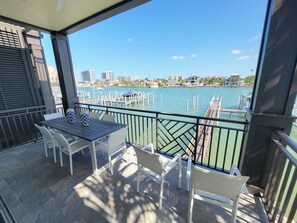 Uma varanda com mesa e cadeiras, com vista para uma marina com barcos e edifícios ao fundo.