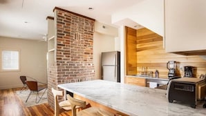 Een moderne keuken met een marmeren aanrecht, houten barstoelen, een geaccentueerde bakstenen muur en een ingebouwde houten kast.
