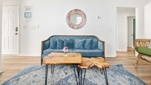 A living room with a blue sofa, a wooden coffee table, and a round mirror on the wall. - Walk Everywhere! Cannon St Retreat! (Charleston)