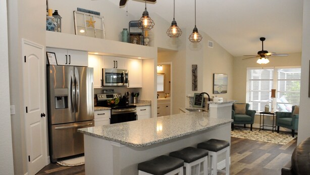 A modern kitchen with stainless steel appliances, a granite island with bar stools, pendant lighting, and a ceiling fan. - Breathtaking 3 Bedroom 2 Bath Private Pool Home in Punta Gorda FL (Punta Gorda)