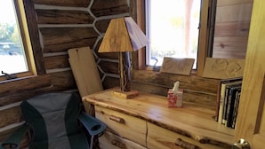 Ein rustikales Holzhäuschen im Inneren mit einem Holztisch, einer Lampe, einem Stuhl und einem Bücherregal.