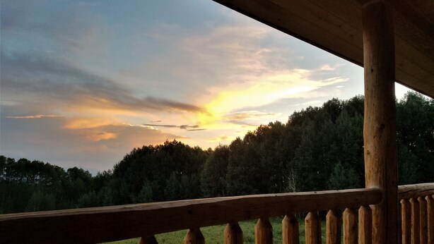 Eine Holzterrasse mit Blick auf einen bewaldeten Hügel und einen Sonnenuntergang.