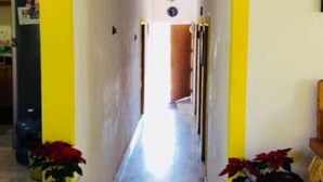Un couloir avec une horloge en bois accrochée au mur, des piliers jaunes et des plantes en pot.