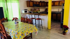 Un coin repas avec une table recouverte d’une nappe à motifs, des chaises en bois et une plante en pot.