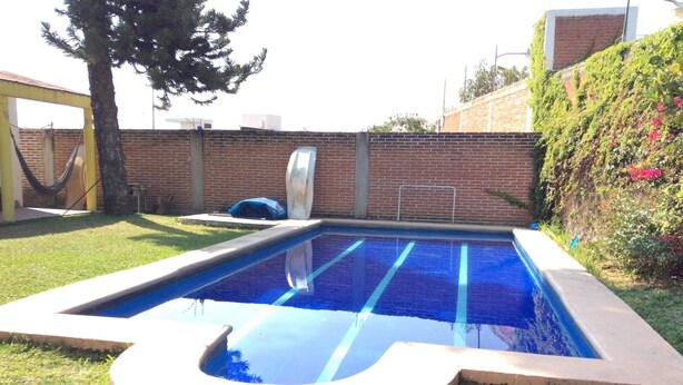 Une piscine rectangulaire à l’intérieur bleu, entourée d’une terrasse en béton et d’un mur en briques.