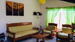Un salon avec un canapé en bois, deux fauteuils en bois, une table basse en bois et un luminaire jaune suspendu au plafond.