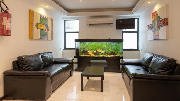 A living room with two black leather sofas, a coffee table, a large fish tank, and artwork on the walls.