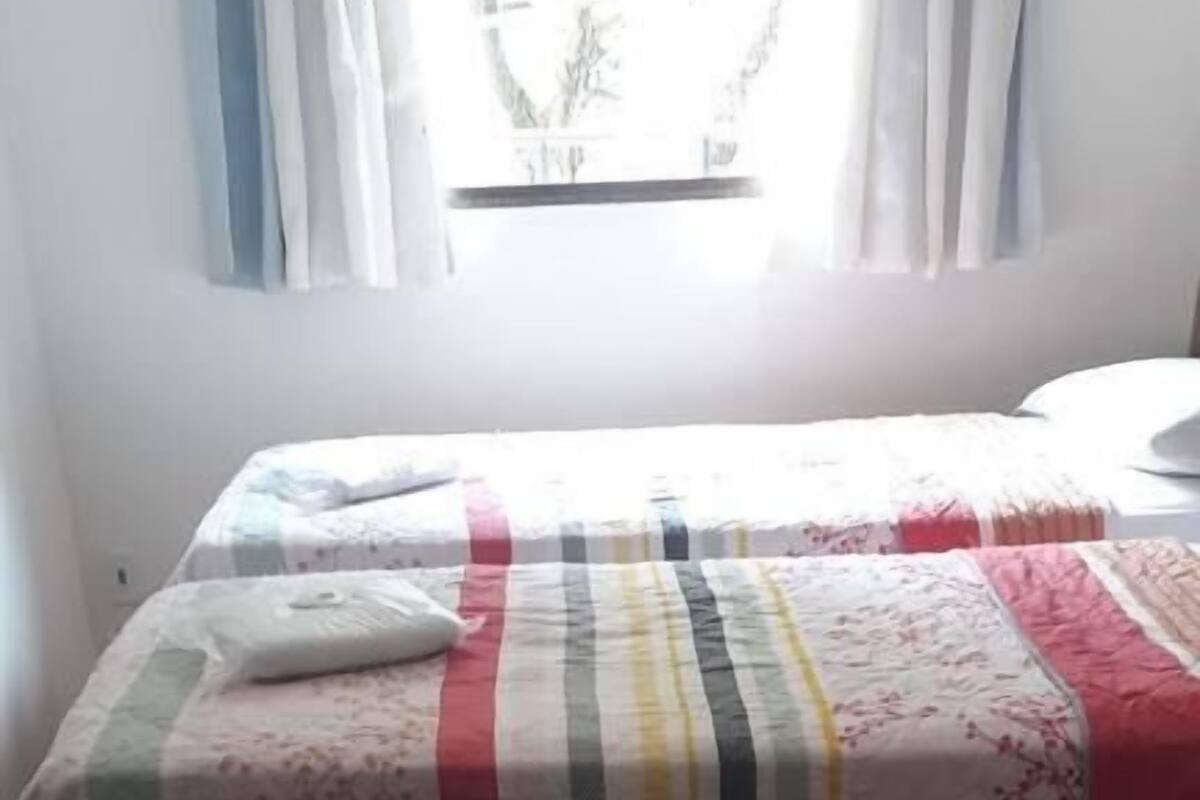 A single bed with a striped bedspread, a pillow, and a window with curtains.