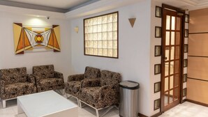 A living room with a sofa set, a coffee table, a trash bin, a window with blinds, and a door with a glass panel.