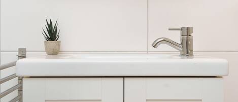 A bathroom with a white sink, a potted plant, and a chrome faucet.