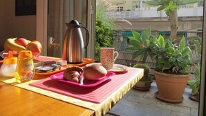 A breakfast setup on a balcony with a table, a coffee pot, a fruit bowl, a muffin tray, and a potted plant. - Ariston (Palermo)
