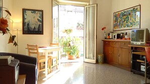 A living room with a sofa, a dining table with chairs, a kitchen area with a TV, and a large window with a view of the outside. - Ariston (Palermo)