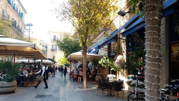 An outdoor café area with tables and chairs, surrounded by buildings and trees. - Ariston (Palermo)