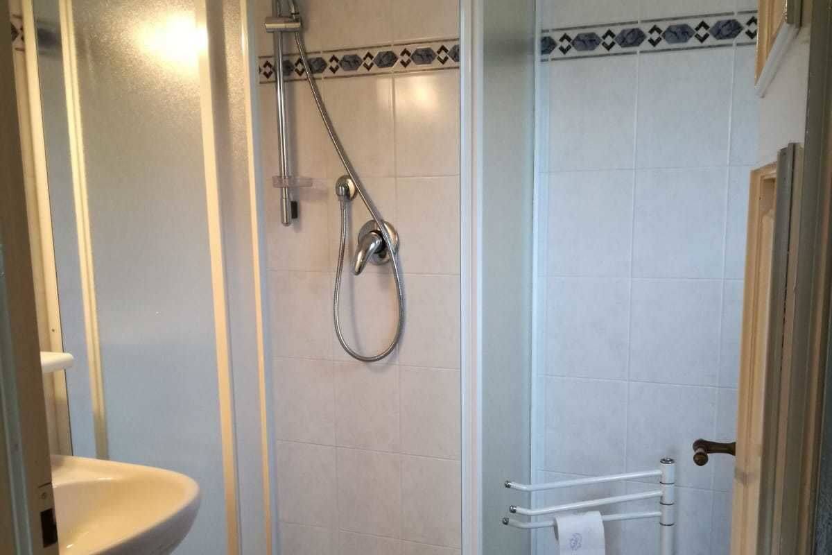 Une douche avec une porte en verre, un lavabo blanc et un porte-serviettes.