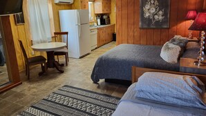 Habitación compacta con cama, una mesita, una silla, kitchenette y televisor.