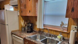 Una cocina con armarios de madera, un lavamanos doble, una cafetera y un refrigerador.