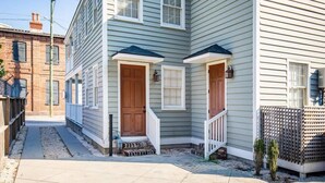 A two-story house with a front porch, a brick wall on the left, and a wooden fence on the right. - 4BR Charleston Single! One Block to King St! (Charleston)