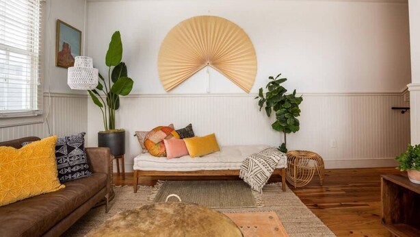 A living room with a sofa, a large fan, a potted plant, and a wooden floor. - 4BR Charleston Single! One Block to King St! (Charleston)