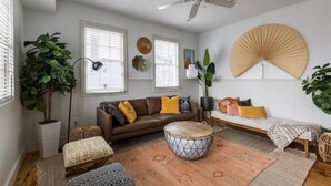 A cozy living room with a brown sofa, a round ottoman, and a ceiling fan. - 4BR Charleston Single! One Block to King St! (Charleston)