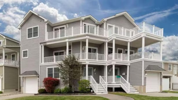 A two-story residential building with a balcony on each floor, a covered front porch, and a small front yard.