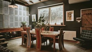 A dining area with a wooden table and chairs, a potted plant, and a view of the outdoors through a window. - The Stables Daylesford ~ Incredible Property! (Daylesford)