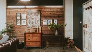 A cozy room with wooden panel walls, a brown leather sofa, a wooden chest of drawers, and a large abstract painting. - The Stables Daylesford ~ Incredible Property! (Daylesford)
