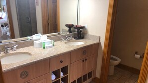 Ein Badezimmer mit zwei Waschbecken, einem großen Spiegel und einer Toilette. Handtücher werden in einem Schrank unter den Waschbecken aufbewahrt.