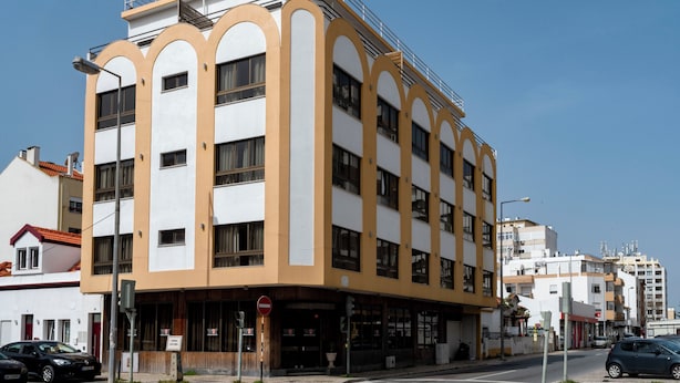 A multi-story building with a white and yellow facade, large windows, and a visible ground floor entrance. - WOT Costa da Caparica Soul (Almada)
