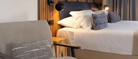 Une chambre d’hôtel avec un lit, une chaise, un bureau, une lampe et deux tableaux encadrés au mur.