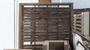 Een balkon met twee beige banken, een houten scheidingswand en uitzicht op een modern gebouw.