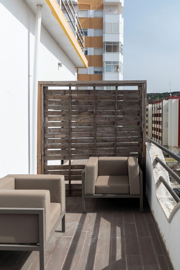 Un balcón con dos sofás color beige, una separación de madera y vista a un edificio moderno.