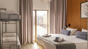 Een hotelkamer met een stapelbed, een eenpersoonsbed, uitzicht door een glazen deur en een houten wand.