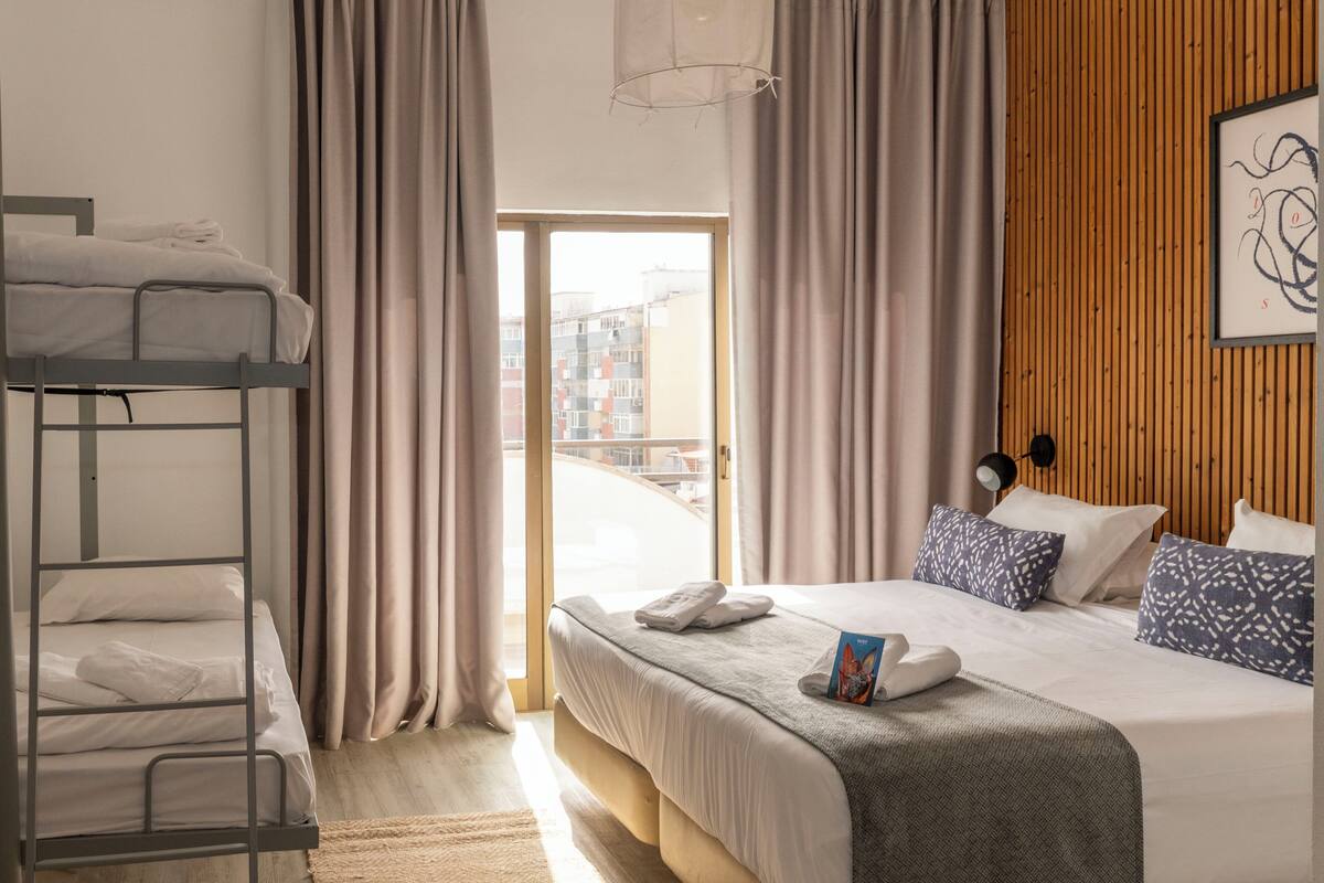 Une chambre d’hôtel avec un lit superposé, un lit simple, une vue à travers une porte vitrée et un mur en bois.