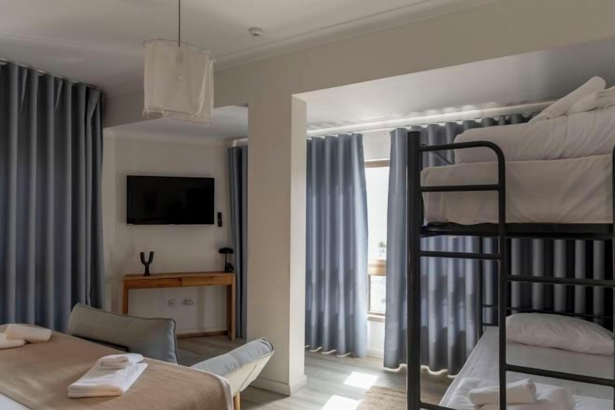 Ein Hotelzimmer mit Etagenbett, Flachbildfernseher, Nachttisch und einem Fenster mit Vorhängen.