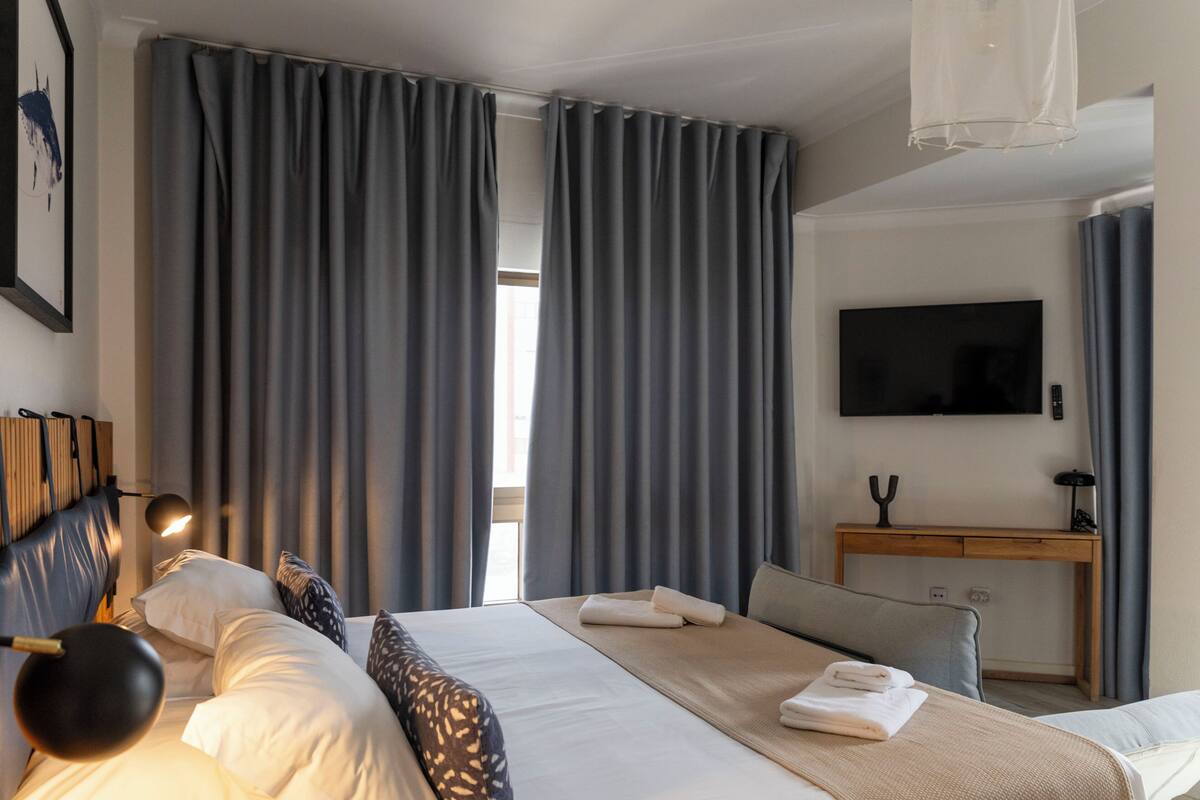 Une chambre d’hôtel équipée d’un lit, d’un bureau, d’un téléviseur à écran plat et d’une grande fenêtre avec des rideaux.