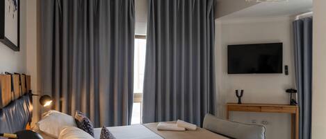 Habitación de hotel con cama, escritorio, televisión de pantalla plana y un amplio ventanal con cortinas.