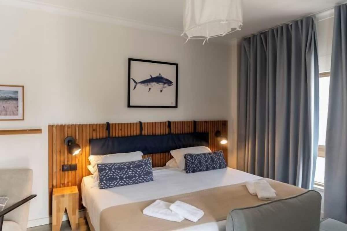 Hotelkamer met een bed, houten hoofdbord, een afbeelding van een haai in een lijst, nachtkastje en een stoel.